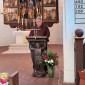 Ein Herr im Pulover spricht vor einem Altar.