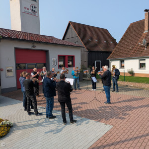 Posaunenchor mit Feuerwehrhaus im Hintergrund.